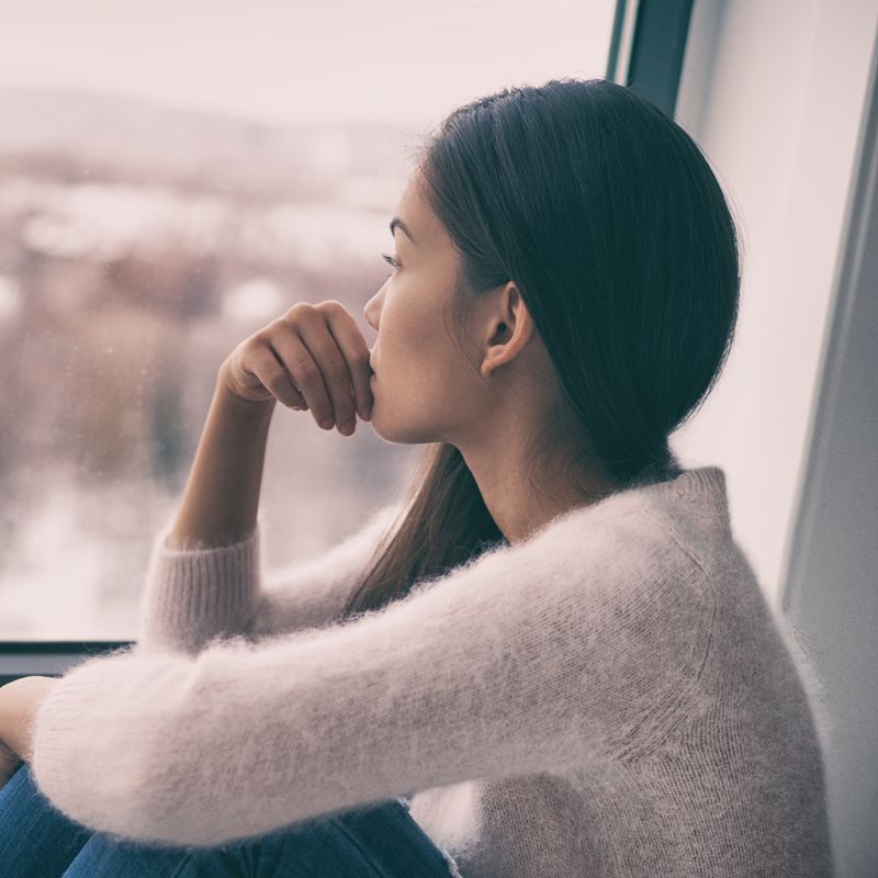 Winter depression - seasonal affective disorder mental health woman sad comtemplative looking out the window alone.