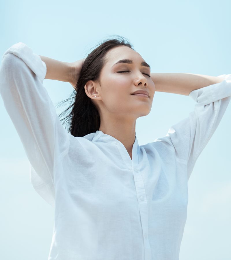 low angle view of young asian woman with closed eyes against blue sky